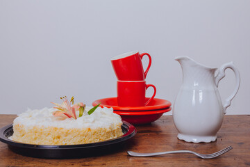 Brazilian coconut cake on a wooden table with dishes and red cups.