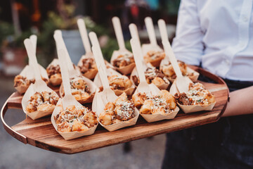 Wooden platter of canapes with bowls and forks held by waitress