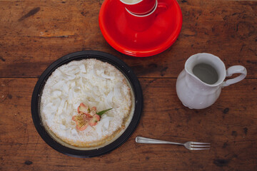 Brazilian coconut cake on a wooden table with dishes and red cups.