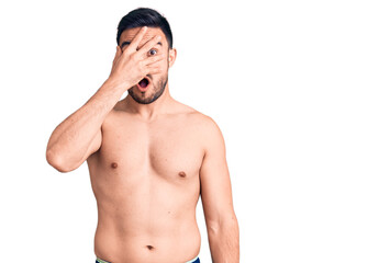 Fototapeta premium Young handsome man wearing swimwear peeking in shock covering face and eyes with hand, looking through fingers with embarrassed expression.