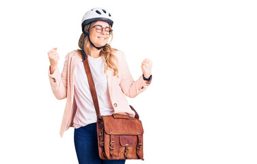 Young caucasian woman wearing bike helmet and leather bag very happy and excited doing winner gesture with arms raised, smiling and screaming for success. celebration concept.