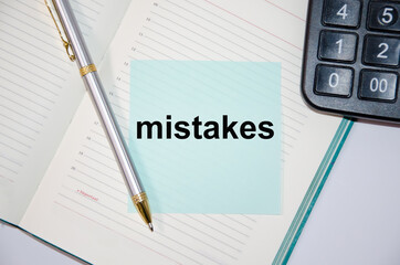 The word mistakes is written on a paper blue block near a calculator and notepad. pen next
