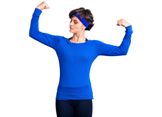 Beautiful young woman with short hair wearing training workout clothes showing arms muscles smiling proud. fitness concept.