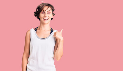 Beautiful young woman with short hair wearing casual sport clothes smiling with happy face looking and pointing to the side with thumb up.