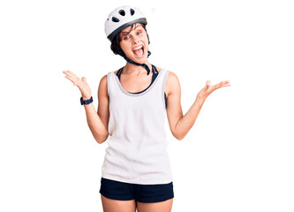 Beautiful young woman with short hair wearing bike helmet celebrating victory with happy smile and winner expression with raised hands