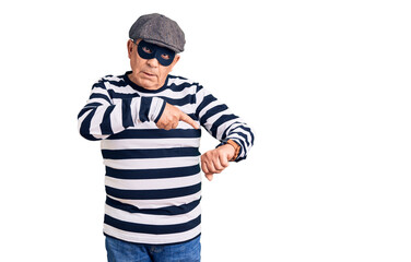 Senior handsome man wearing burglar mask and t-shirt in hurry pointing to watch time, impatience, upset and angry for deadline delay