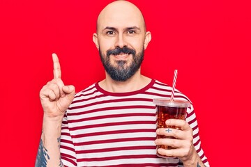 Young handsome man drinking glass of cola beverage surprised with an idea or question pointing finger with happy face, number one