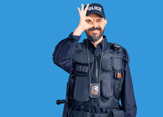 Young handsome man wearing police uniform doing ok gesture with hand smiling, eye looking through fingers with happy face.