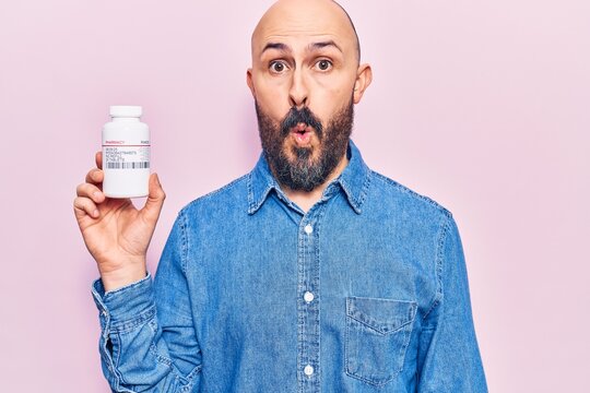 Young handsome man holding pills scared and amazed with open mouth for surprise, disbelief face