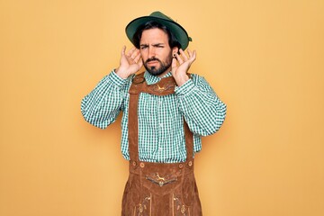 Young handsome man wearing tratidional german octoberfest custome for Germany festival Trying to hear both hands on ear gesture, curious for gossip. Hearing problem, deaf