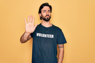 Young handsome hispanic volunteer man wearing volunteering t-shirt as social care doing stop sing with palm of the hand. Warning expression with negative and serious gesture on the face.