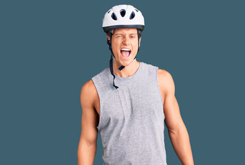 Young handsome man wearing bike helmet winking looking at the camera with sexy expression, cheerful...
