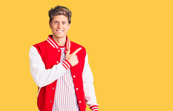 Young handsome man wearing baseball uniform cheerful with a smile on face pointing with hand and finger up to the side with happy and natural expression