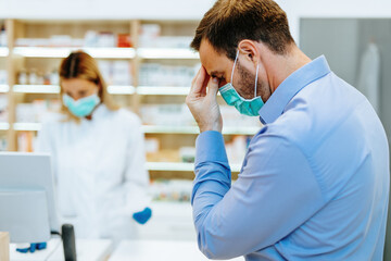 Customer with protective mask on his face buying pills in modern drugstore.