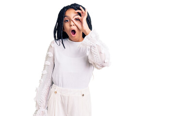 Cute african american girl wearing casual white tshirt doing ok gesture shocked with surprised face, eye looking through fingers. unbelieving expression.