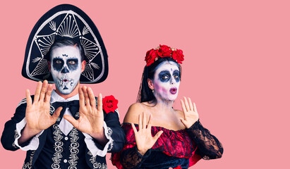 Young couple wearing mexican day of the dead costume over background moving away hands palms showing refusal and denial with afraid and disgusting expression. stop and forbidden.