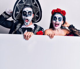 Young couple wearing mexican day of the dead costume holding blank empty banner crazy and scared with hands on head, afraid and surprised of shock with open mouth