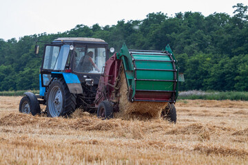 Obraz premium tractor makes big straw roll on yellow field at summer day