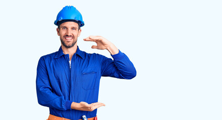 Young handsome man wearing worker uniform and hardhat gesturing with hands showing big and large size sign, measure symbol. smiling looking at the camera. measuring concept.