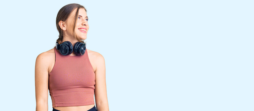 Beautiful caucasian young woman wearing gym clothes and using headphones looking away to side with smile on face, natural expression. laughing confident.