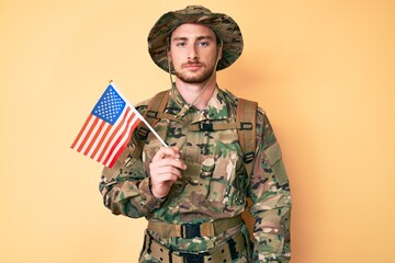 Young caucasian man wearing camouflage army uniform holding usa flag thinking attitude and sober expression looking self confident