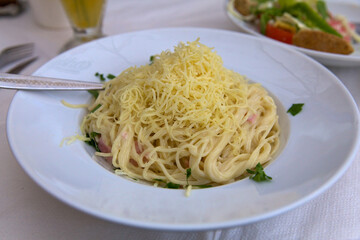 Close-up of food in a restaurant on the island of Crete. Carbonara pasta, sprinkled with grated cheese and garnished with herbs, on a large white plate
