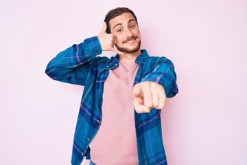 Young handsome man wearing casual clothes smiling doing talking on the telephone gesture and pointing to you. call me.