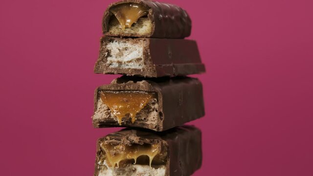 Four candy bars spin on pink background. The unpacked sweets close up macro shot. Nougat and caramel inside chocolate bars.