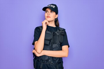 Young police woman wearing security bulletproof vest uniform over purple background with hand on chin thinking about question, pensive expression. Smiling and thoughtful face. Doubt concept.