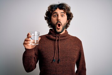 Young handsome man with beard drinking glass of water over isolated white background scared in...