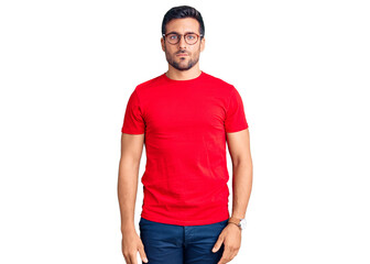 Young hispanic man wearing casual clothes and glasses with serious expression on face. simple and...