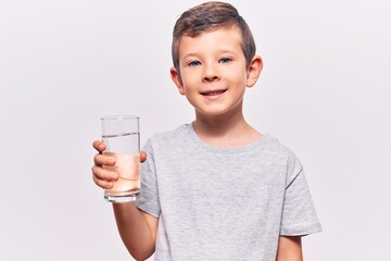 Cute blond kid drinking glass of water looking positive and happy standing and smiling with a confident smile showing teeth
