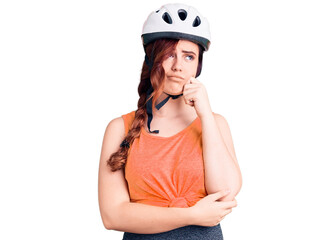 Young beautiful woman wearing bike helmet serious face thinking about question with hand on chin, thoughtful about confusing idea