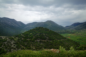 Fototapeta premium Natural landscape on the island of Crete in Greece, with views of a large green hill, meadows and mountains, in cloudy weather