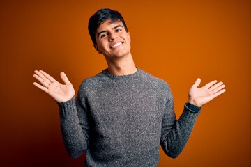 Young handsome man wearing casual sweater standing over isolated orange background clueless and...