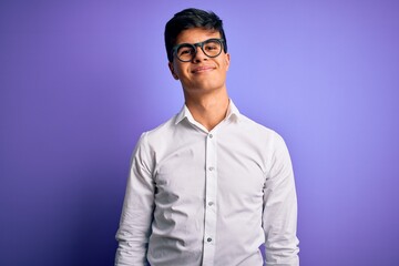 Obraz premium Young handsome business man wearing shirt and glasses over isolated purple background Relaxed with serious expression on face. Simple and natural looking at the camera.