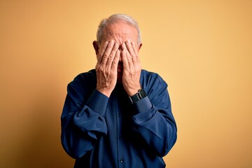 Grey haired senior man wearing casual blue shirt standing over yellow background with sad...