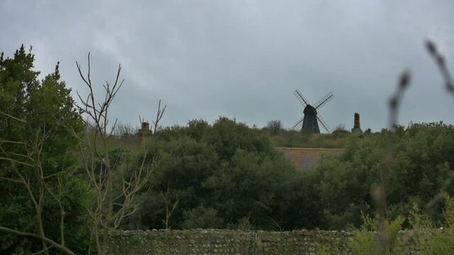 View over the trees and rooftops towards a classic old windmill perched on a hill in the south of England