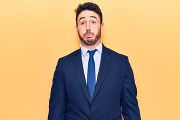 Young hispanic man wearing suit puffing cheeks with funny face. mouth inflated with air, crazy expression.