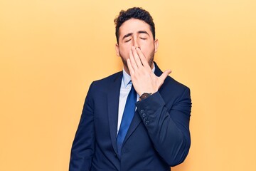 Young hispanic man wearing suit bored yawning tired covering mouth with hand. restless and sleepiness.