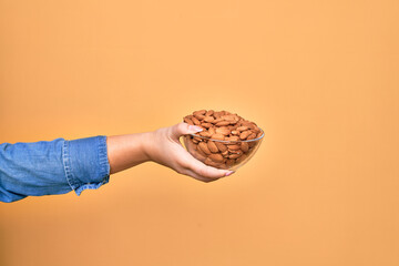 Beautiful hand of woman holding bowl with baked german pretzels over isolated yellow background