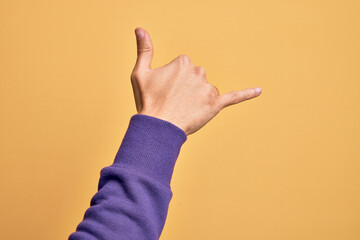 Hand of caucasian young man showing fingers over isolated yellow background gesturing Hawaiian shaka greeting gesture, telephone and communication symbol