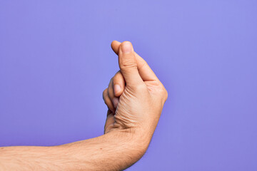 Hand of caucasian young man showing fingers over isolated purple background holding blank space with thumb finger, business and advertising