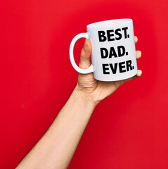 Beautiful hand of man holding cup of coffee with best dad ever message over isolated red background