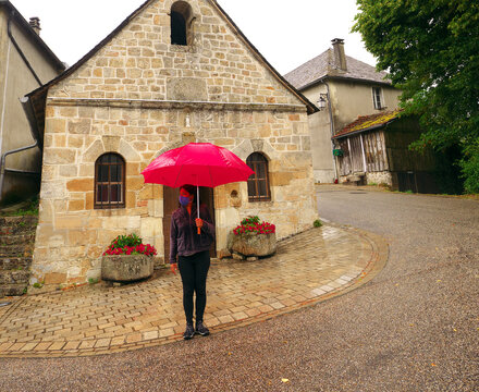 A woman wearing a mask is waiting with an umbrella