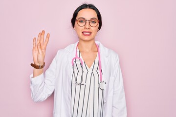 Beautiful doctor woman with blue eyes wearing coat and stethoscope over pink background showing and pointing up with fingers number four while smiling confident and happy.