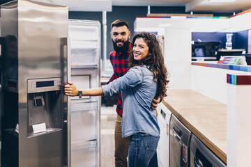 Fototapeta na wymiar Young couple, satisfied customers choosing fridge in appliances store.