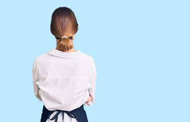 Beautiful brunette young woman wearing professional waitress apron standing backwards looking away...