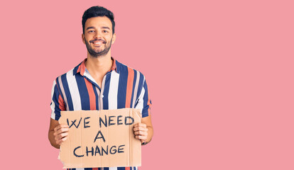 Young handsome hispanic man holding we need a change banner looking positive and happy standing and...