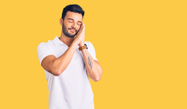 Young handsome hispanic man wearing casual clothes sleeping tired dreaming and posing with hands together while smiling with closed eyes.